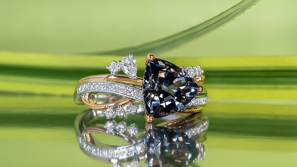 Trillion-cut grey spinel embraced by a curving diamond pave band in yellow gold, featuring custom-cut diamonds along the rim of the band.